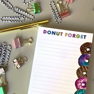 May include: A white notepad with the text "DONUT FORGET" in rainbow colors. The notepad has lined paper and a border of colorful donuts on the right side.
