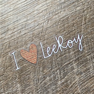 May include: A clear sticker with the text "I love Leekoy" in white lettering. A red heart with a brick pattern is behind the "I".