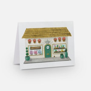 May include: A white building with a green door and a sign that says "The Flower Shop". There are flowers in pots hanging from the building and a sign that says "Fresh Flowers".
