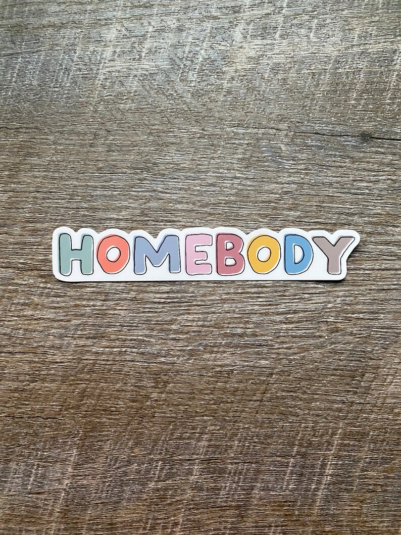 May include: A sticker with the word "HOMEBODY" in colorful letters. The letters are outlined in white and have a slightly raised, 3D effect.
