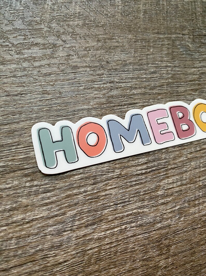 May include: A sticker with the word "HOMEBODY" in colorful, outlined letters. The letters are in different colors, including green, orange, blue, pink, and yellow.