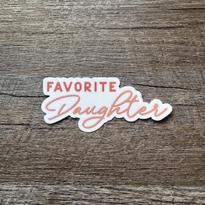 May include: White sticker with the text "FAVORITE Daughter" in pink cursive lettering.
