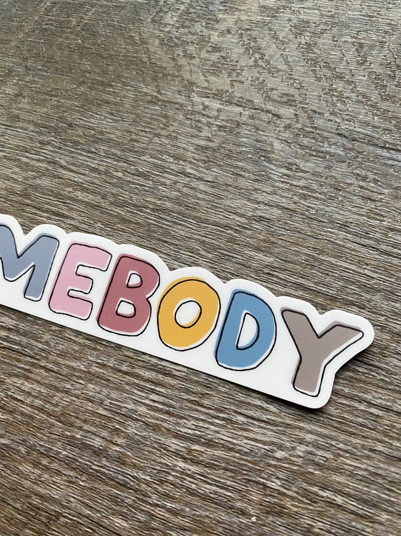May include: A sticker with the word "somebody" written in colorful, outlined letters. The letters are in shades of gray, pink, red, yellow, blue, and brown.
