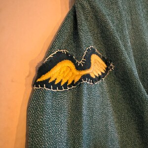 May include: A green denim jacket with a yellow embroidered wing patch sewn onto the sleeve.