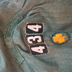 May include: A green fabric patch with the text "Girl Scouts" and the numbers "434" in white on black patches. A yellow four-leaf clover patch is on the right.