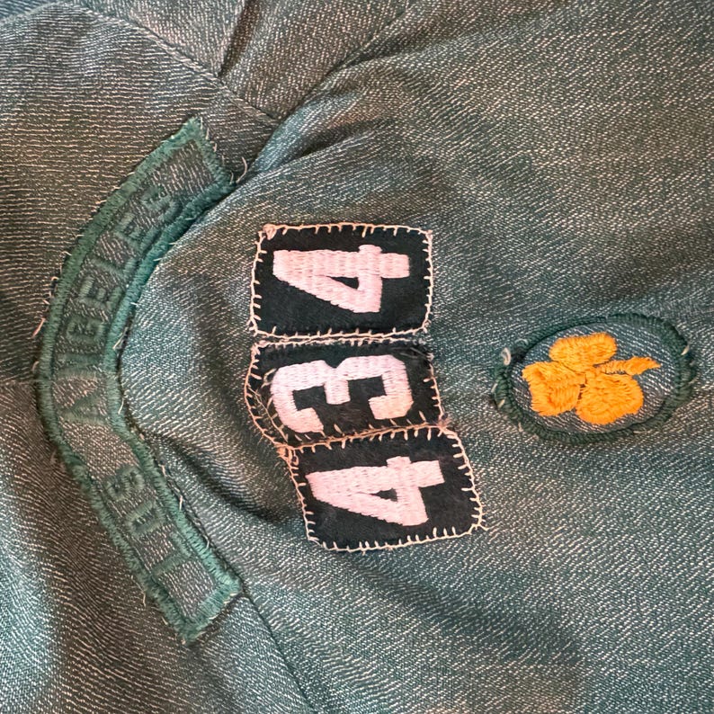 May include: A green fabric patch with the text "Girl Scouts" and the numbers "434" in white on black patches. A yellow four-leaf clover patch is on the right.