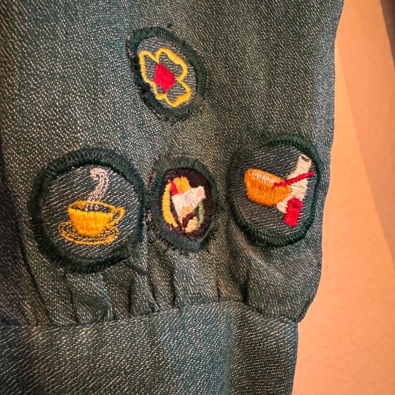 May include: Green fabric with four embroidered patches. The patches are circular and feature a flower, a cup of coffee, a bird, and a spoon and bowl.