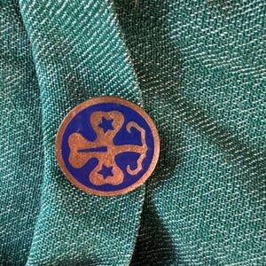 May include: A blue and gold Girl Scout pin with a four-leaf clover design and three stars.