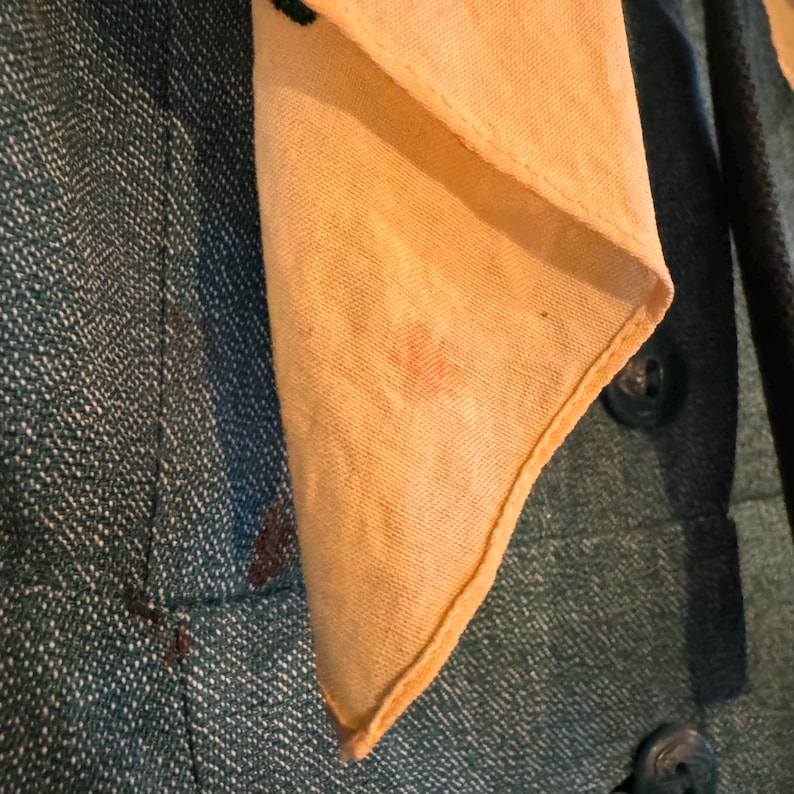 May include: A close-up of a teal blue fabric with a light yellow fabric folded over it. The yellow fabric has a small pink stain.