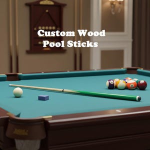 May include: A pool table with a green felt surface, a cue stick, and a set of billiard balls. The cue stick is green and cream-colored. The text "Custom Wood Pool Sticks" is displayed in white.