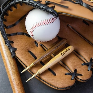 May include: A brown leather baseball glove with a white baseball and two wooden baseball bats with the names "James" and "Olivia" engraved on them.