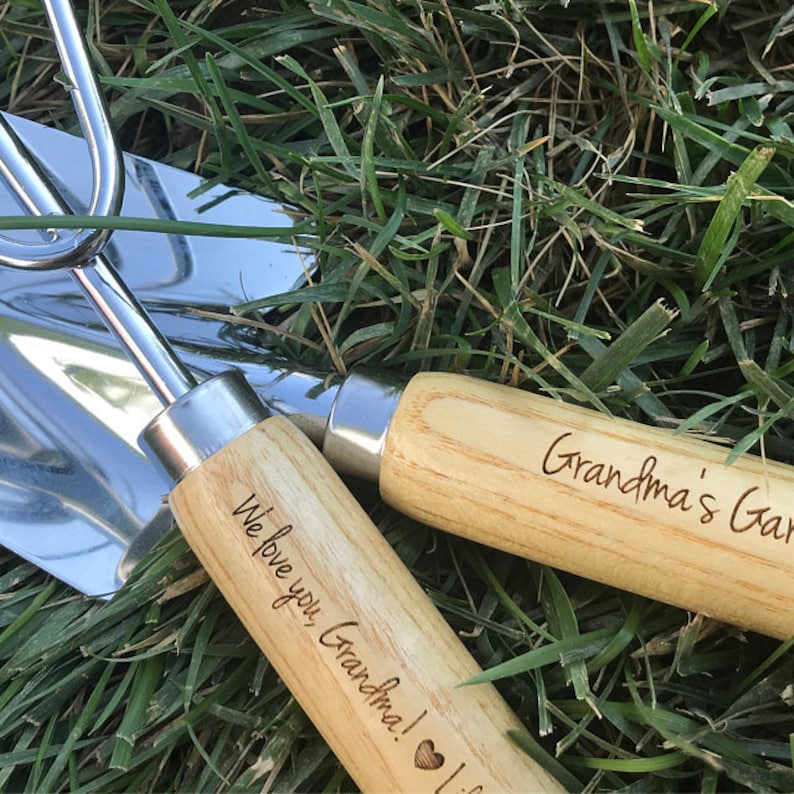 May include: A set of two gardening tools with wooden handles. The handles are engraved with the text "We love you Grandma!" and "Grandma's Garden".