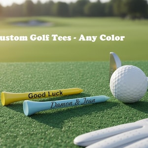 May include: Image of custom golf tees in yellow and light blue, with text that reads "Good Luck" and "Damon & Jean". A golf ball, club, and glove are also visible on the green turf. The text "Custom Golf Tees - Any Color" is at the top.
