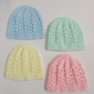 Op de afbeelding: Vier gebreide baby mutsjes in verschillende kleuren: lichtblauw, lichtgroen, geel en roze. De mutsjes hebben een textuurpatroon en zijn gemaakt van zacht garen.