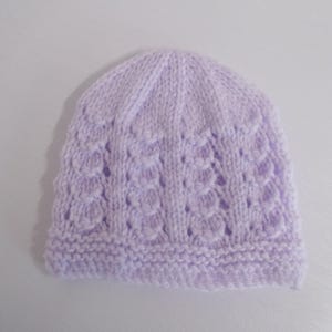 Op de afbeelding: Een gebreide baby muts in lavendelkleur met een delicaat opengewerkt patroon.