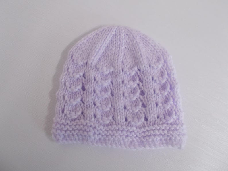 Op de afbeelding: Een gebreide baby muts in lavendelkleur met een delicaat opengewerkt patroon.