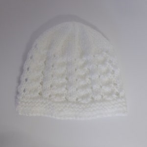 Op de afbeelding: Witte gebreide baby muts met een kantpatroon.