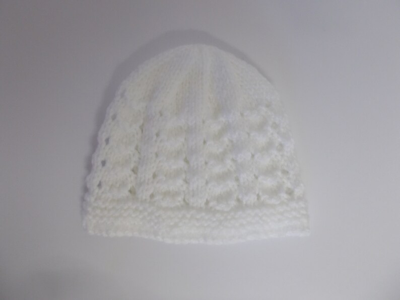 Op de afbeelding: Witte gebreide baby muts met een kantpatroon.