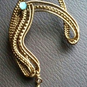 May include: A gold wire wrapped ear cuff with two light blue crystal beads. The ear cuff is shaped like a crescent moon and has a delicate, intricate design.