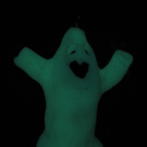 Op de afbeelding: Een groen, in het donker lichtend spookfiguur met een vriendelijk gezicht en uitgestrekte armen.