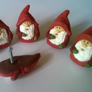 May include: Five red and white gnome-shaped cabinet knobs with green accents. The knobs are arranged in a semi-circle on a white surface. One knob is missing its screw.