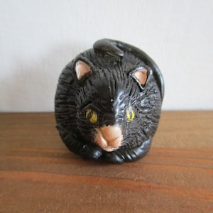 Peut inclure: Une petite figurine de chat en céramique noire avec des yeux jaunes. Le chat est enroulé dans une position de sommeil.