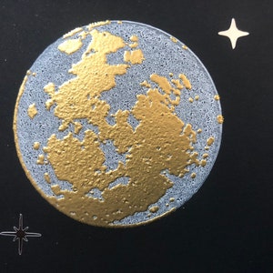 Puede incluir: Una luna dorada y blanca con una superficie texturizada sobre un fondo negro con estrellas blancas.