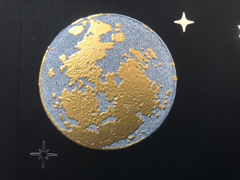 Puede incluir: Una luna dorada y blanca con una superficie texturizada sobre un fondo negro con estrellas blancas.