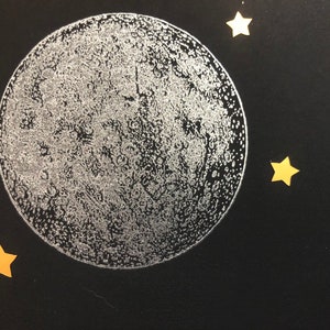 Puede incluir: Una luna plateada con una textura de superficie detallada sobre un fondo negro con cuatro estrellas doradas.