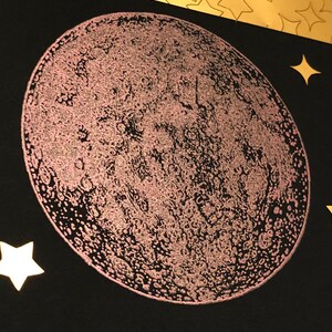 Puede incluir: Primer plano de una luna rosa brillante sobre un fondo negro. La luna es una ilustraci&oacute;n detallada con cr&aacute;teres y otras caracter&iacute;sticas de la superficie.