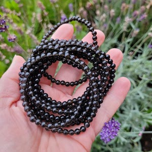 May include: A strand of black gemstone beads, possibly obsidian or smoky quartz, arranged in a coil. The beads are smooth and polished, with a slight sheen.