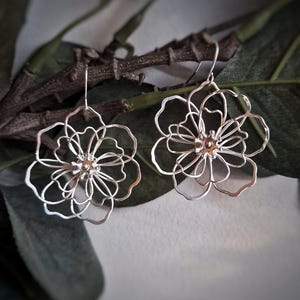 May include: A pair of silver flower-shaped earrings with delicate wirework details.