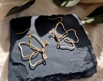 May include: A pair of gold-toned butterfly earrings made of wire. The earrings are delicate and have a simple design.