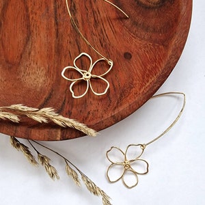 May include: A pair of gold flower-shaped earrings with a delicate wire design. The earrings are suspended from a thin wire loop.