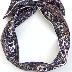 May include: A patterned headband with a knotted top. The fabric features a repeating design of white, brown, and blue floral and geometric shapes. The headband is a stylish accessory.
