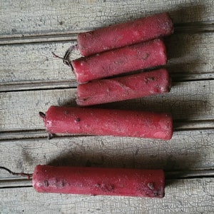 May include: Five red candles on a wooden surface. The candles are all the same size and shape, and they are all slightly worn.