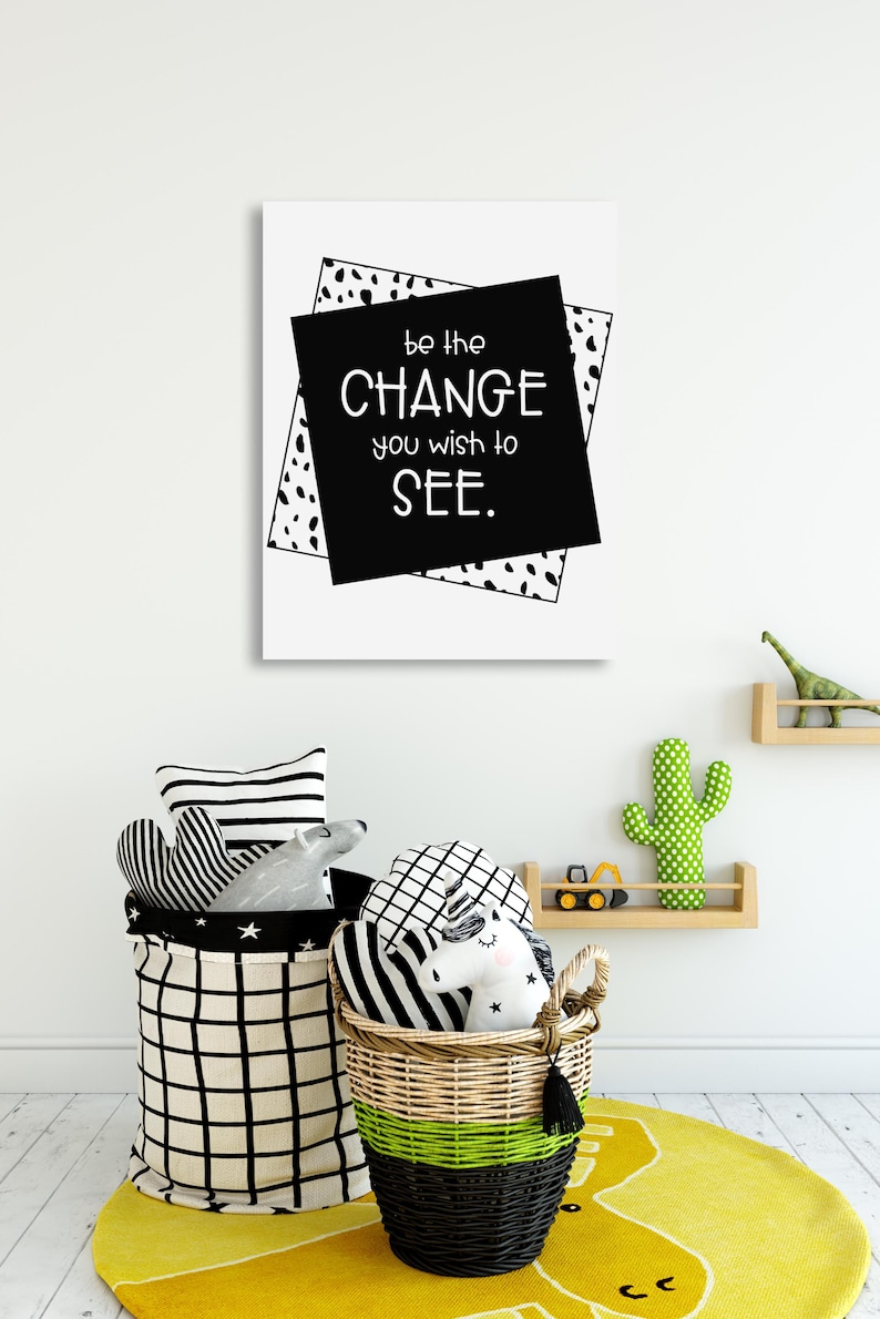 Op de afbeelding: Zwart-witte inspirerende quote print met de tekst "Wees de verandering die je in de wereld wilt zien." De print is ingelijst met een zwart-wit geometrisch patroon.