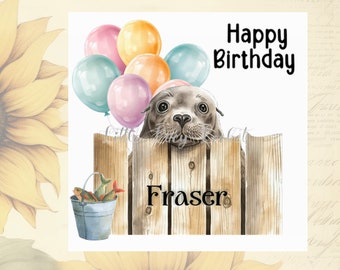 Puede incluir: Una tarjeta de cumpleaños con una foca de dibujos animados mirando por encima de una valla de madera con globos y un cubo de pescado. La tarjeta dice "Feliz cumpleaños Fraser".