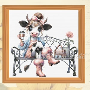 May include: A black and white cow with pink accents sits on a wrought iron bench holding a cup of coffee. The cow is wearing a blue denim jacket and a pink bow.