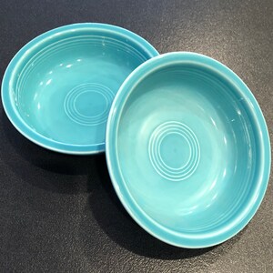 May include: Two turquoise ceramic bowls with a concentric circle design. The bowls are empty and sitting on a black surface.