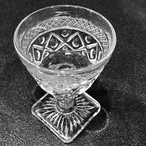 May include: A clear glass cup with a cut glass design. The cup has a square base and a round bowl.