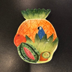 May include: A ceramic pineapple-shaped serving dish with a blue parrot, watermelon, orange, and kiwi fruit designs.