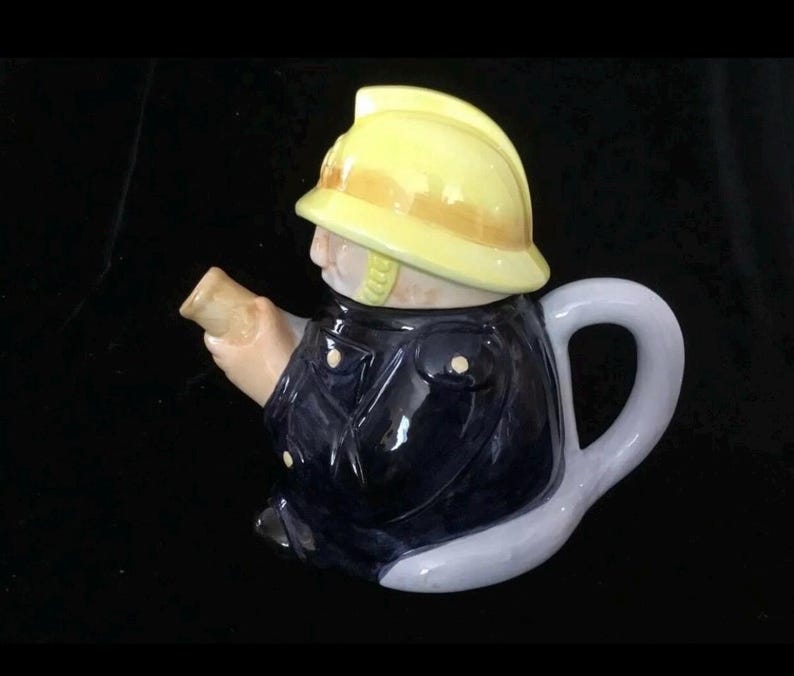 Puede incluir: Tetera de cer&aacute;mica con forma de bombero. La tetera presenta un casco amarillo, una chaqueta azul marino y un asa gris claro. El pico est&aacute; dise&ntilde;ado para parecerse a una manguera. Art&iacute;culo decorativo.