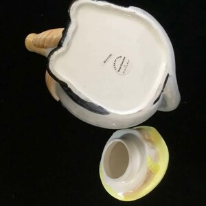 Puede incluir: Una tetera de cer&aacute;mica con tapa, cuerpo blanco con detalles grises y negros. El pico es de color beige y la tapa amarilla y blanca. La tetera tiene una forma y un dise&ntilde;o &uacute;nicos, perfectos para servir t&eacute;.