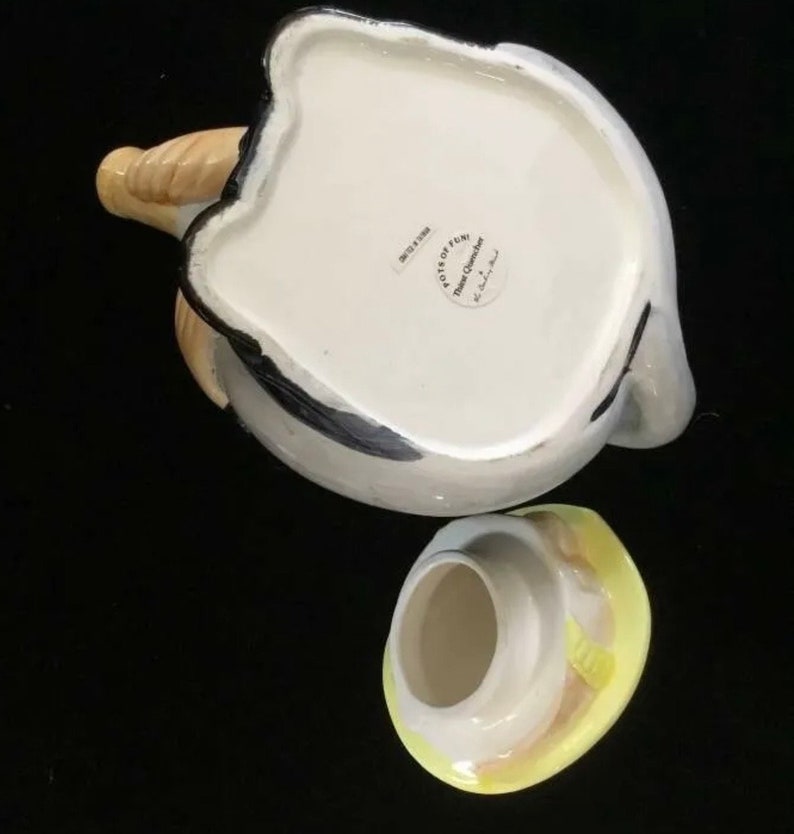 Puede incluir: Una tetera de cer&aacute;mica con tapa, cuerpo blanco con detalles grises y negros. El pico es de color beige y la tapa amarilla y blanca. La tetera tiene una forma y un dise&ntilde;o &uacute;nicos, perfectos para servir t&eacute;.