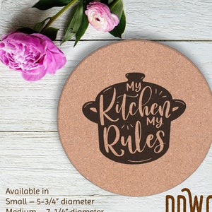 Puede incluir: Un posavasos de corcho marrón con el texto "My Kitchen My Rules" en letras negras dentro de una silueta negra de una olla. El posavasos está disponible en dos tamaños: 5-3/4" de diámetro y 7-1/4" de diámetro. El texto "DDWORKS" está en letras marrones debajo del posavasos.