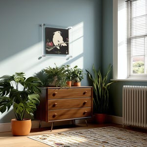 May include: A wooden three-drawer dresser with tapered legs, topped with three potted green plants and a framed print of a white cockatoo on a branch. The dresser is positioned against a blue wall next to a window and a radiator.
