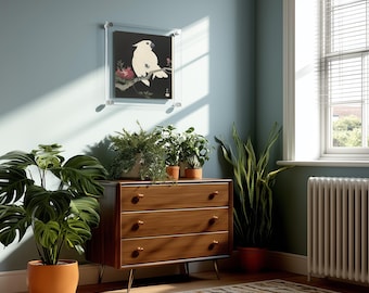 May include: A wooden three-drawer dresser with tapered legs, topped with three potted green plants and a framed print of a white cockatoo on a branch. The dresser is positioned against a blue wall next to a window and a radiator.