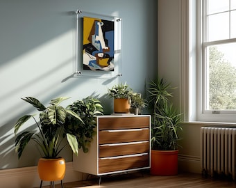 May include: A three-drawer chest with a white frame and wood-grain drawer fronts, featuring silver handles. It is positioned near a wall with a framed abstract painting, several potted plants in orange and yellow planters, and a striped rug.