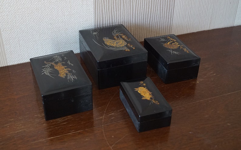 May include: Four black lacquered boxes with gold and silver painted designs. The boxes are of varying sizes and feature different Japanese-inspired motifs.